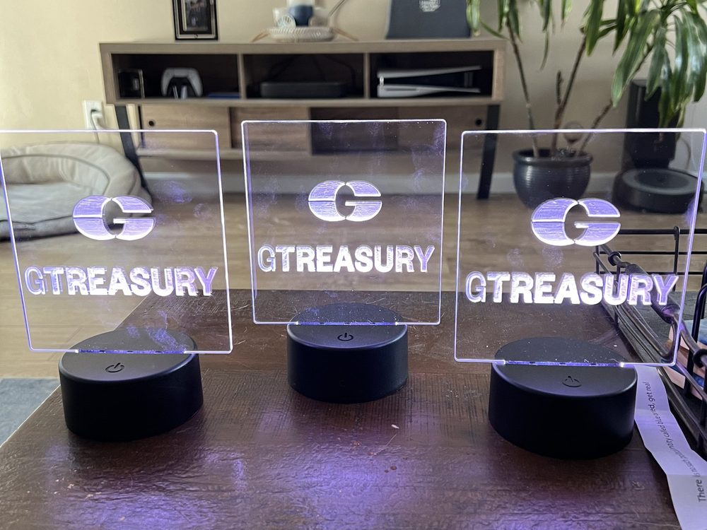 Three engraved acrylic panels lit white on LED bases, each carrying a corporate logo