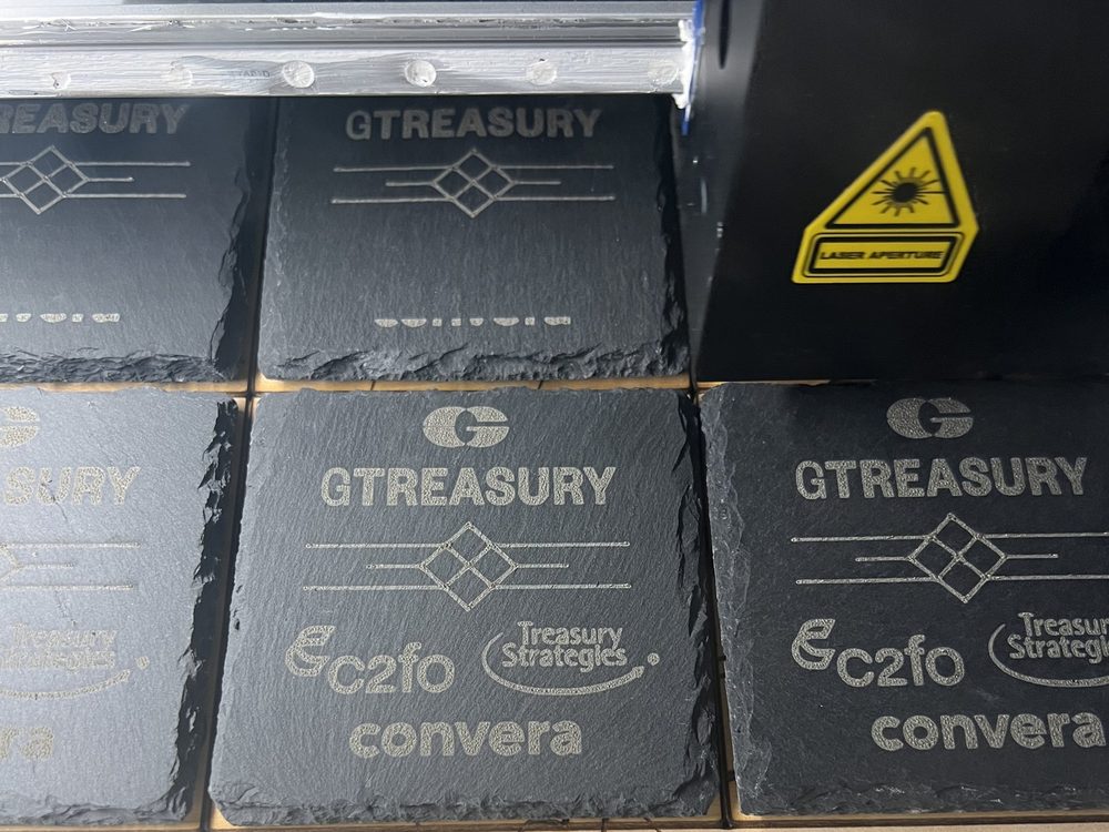 Stacks of laser-engraved slate coasters branded for several corporate clients, on the laser bed