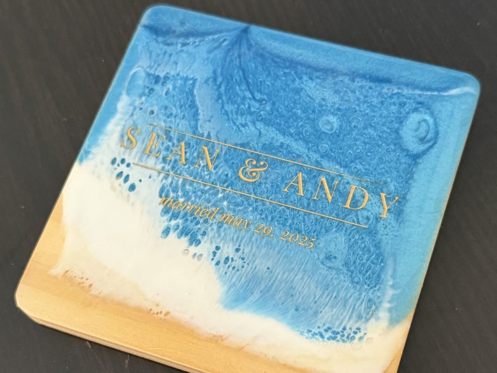 A wood and ocean resin coaster engraved in gold with a couple's names and their wedding date